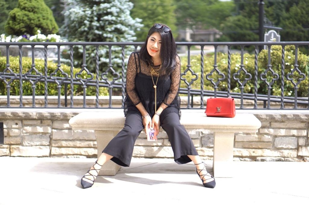 Grace in a black lace top and palazzo pants with laceup flats and a red purse